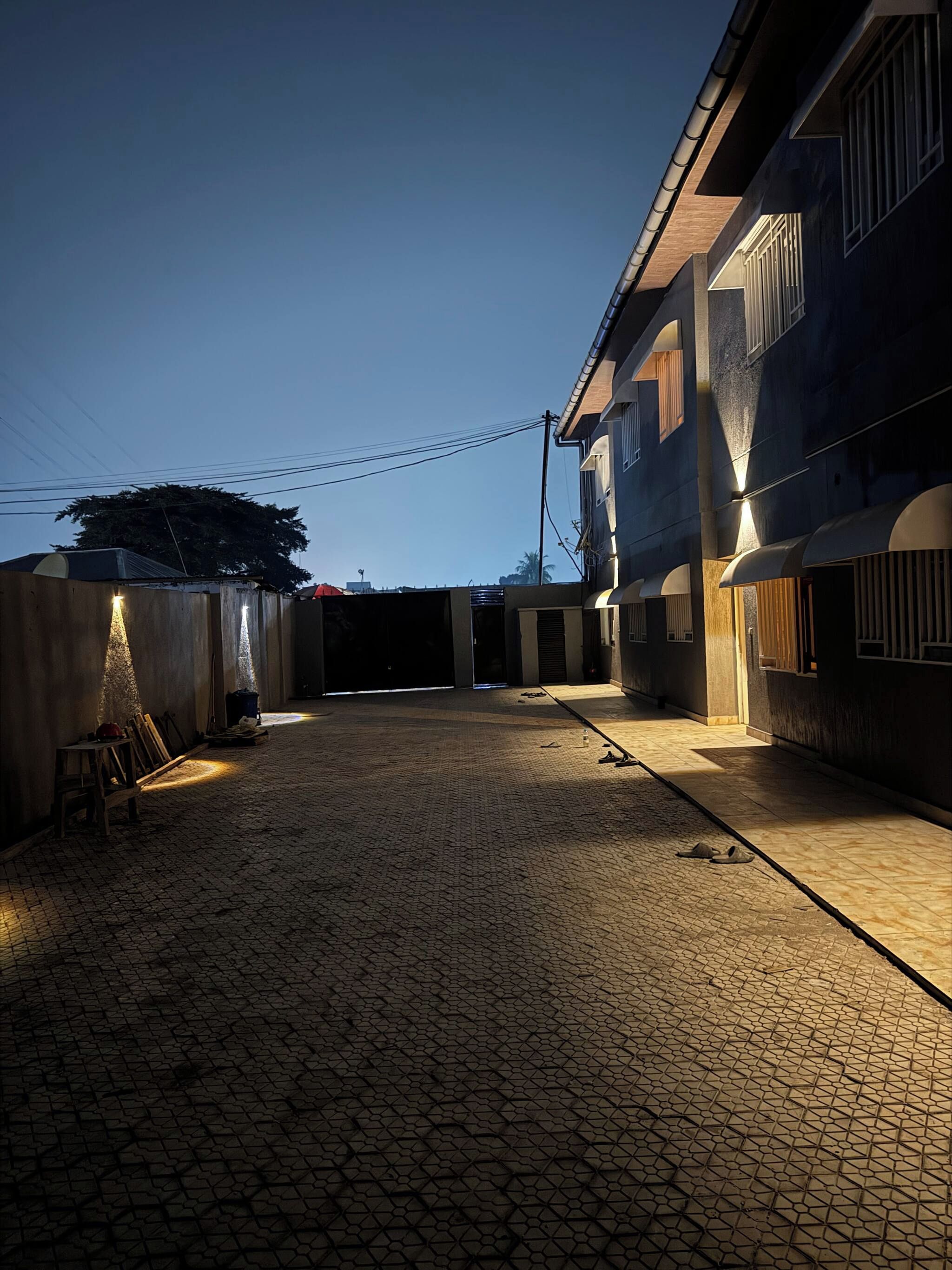 A courtyard with a cobblestone floor, a wooden bench, and a building with a dark facade and windows.