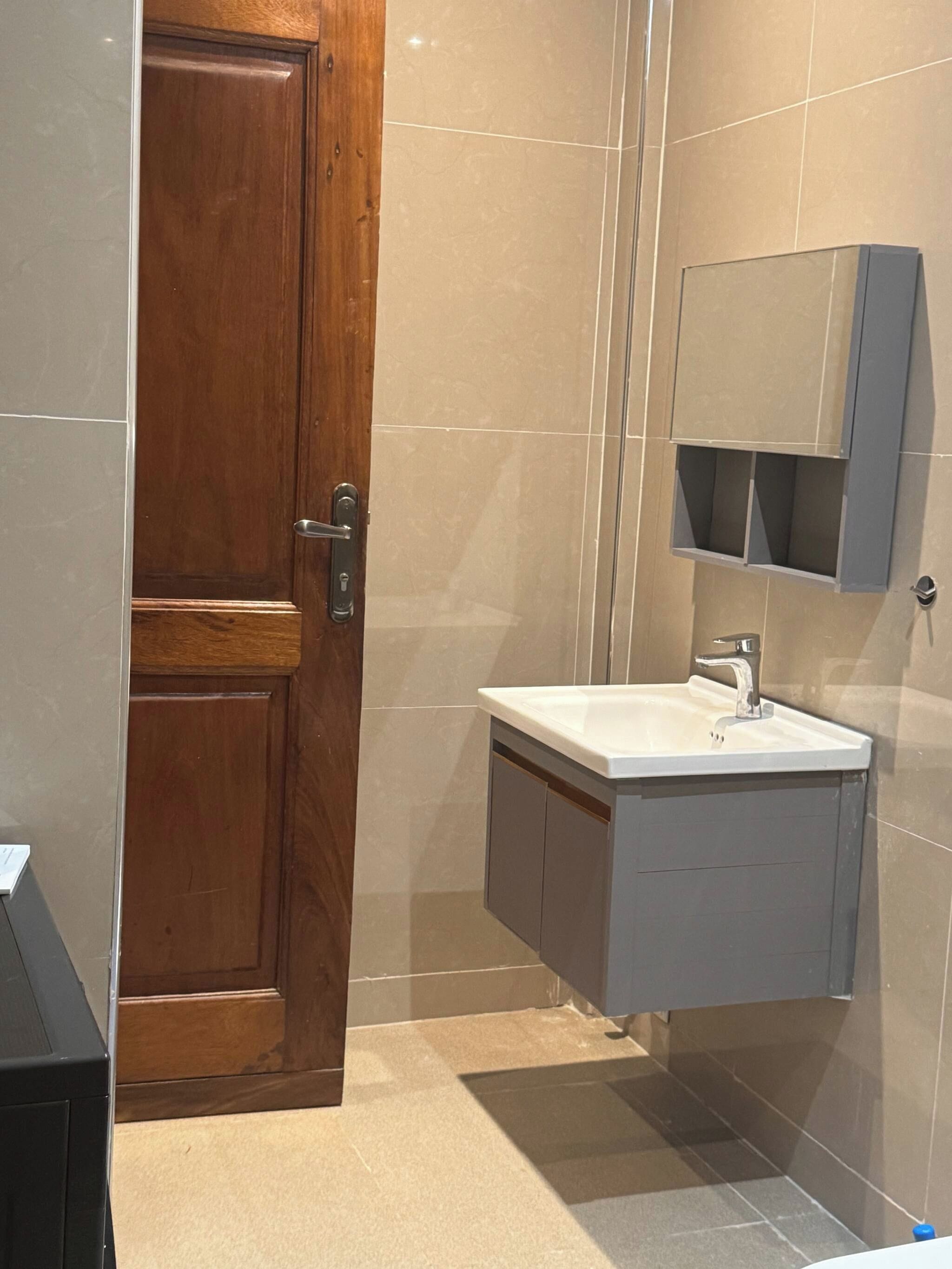 A bathroom with a wooden door, a sink with a mirror, and tiled walls.