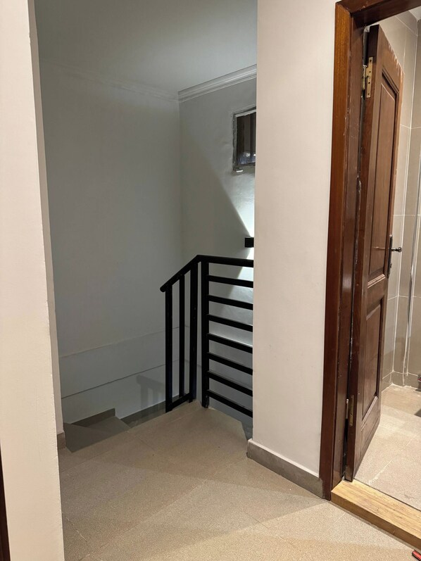 A narrow stairway with a wooden handrail and a closed door at the top.