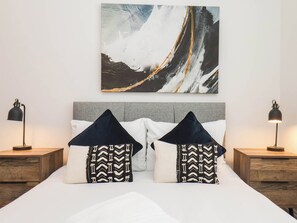 Ein Schlafzimmer mit einem großen Bett, zwei Nachttischen und einem an der Wand befestigten abstrakten Gemälde.