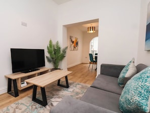 A modern living room with a flat-screen TV, a wooden coffee table, a grey sofa, and a green plant. - Holmwood (Whitby)