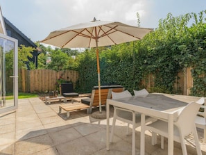 Eine Terrasse im Freien mit Tisch und Stühlen, einer Holzbank, einem Grill und einem großen Sonnenschirm.