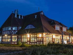 Ein großes, zweistöckiges Gebäude mit einem steilen Walmdach, zahlreichen Schornsteinen und einer Kombination aus Fachwerkkonstruktion und Backstein.