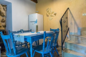 A dining area with a white table and blue chairs, a white refrigerator, and a staircase with a black railing. - Holiday house with garden, grill and boat mooring (Barbat na Rabu)