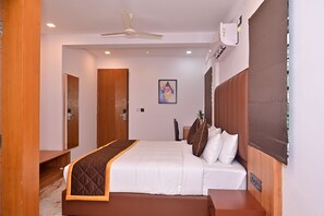 A hotel room with a bed, bedside table, wardrobe, ceiling fan, air conditioning unit, and a painting on the wall. - Bliss Hotel (Bengaluru)