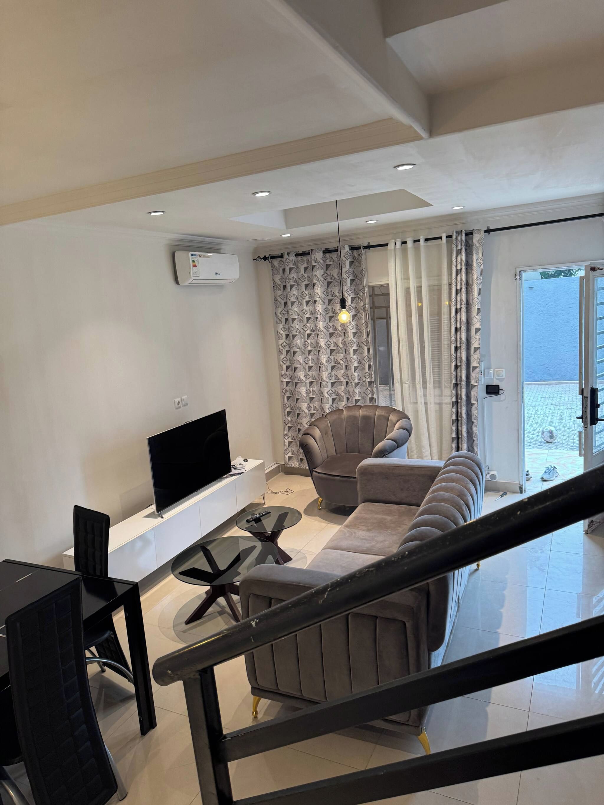 Una sala moderna con un televisor de pantalla plana, un sofá, una mesa de comedor con sillas y una escalera.