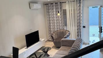 Una sala moderna con un televisor de pantalla plana, un sofá, una mesa de comedor con sillas y una escalera.