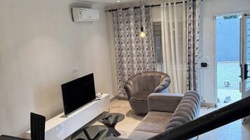 Ein modernes Wohnzimmer mit Fernseher, einer Couch, einem Esstisch mit Stühlen und einer Treppe.