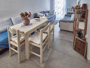 A dining area with a table, chairs, a vase of flowers, and a sofa in the background. - Country House 'The Methana Lookout' with Sea View and Air Conditioning (Μέθανα)