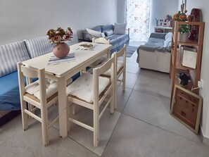 A room with a dining table, chairs, a sofa, and a bookshelf.