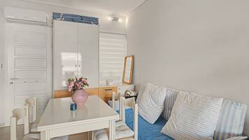 Een kamer met een witte tafel, stoelen, een bank met gestreepte kussens, een roze vaas met bloemen en een witte garderobe met spiegel.