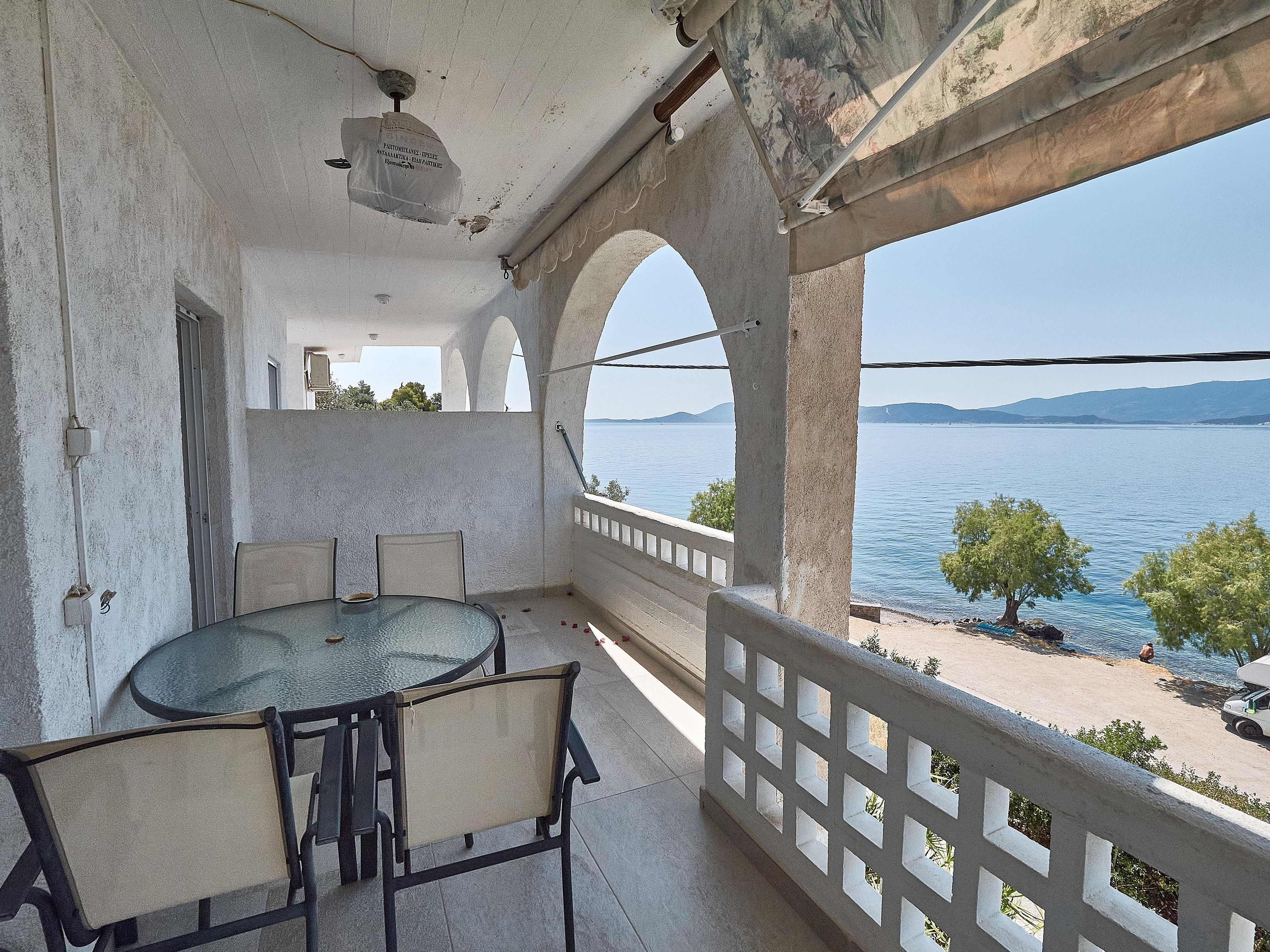 A balcony with a round table and chairs, overlooking a body of water and distant hills.