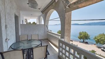 A balcony with a round table and chairs, overlooking a body of water and distant hills.