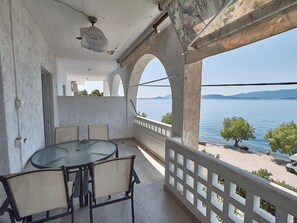 A balcony with a round table and chairs, overlooking a body of water and distant hills.