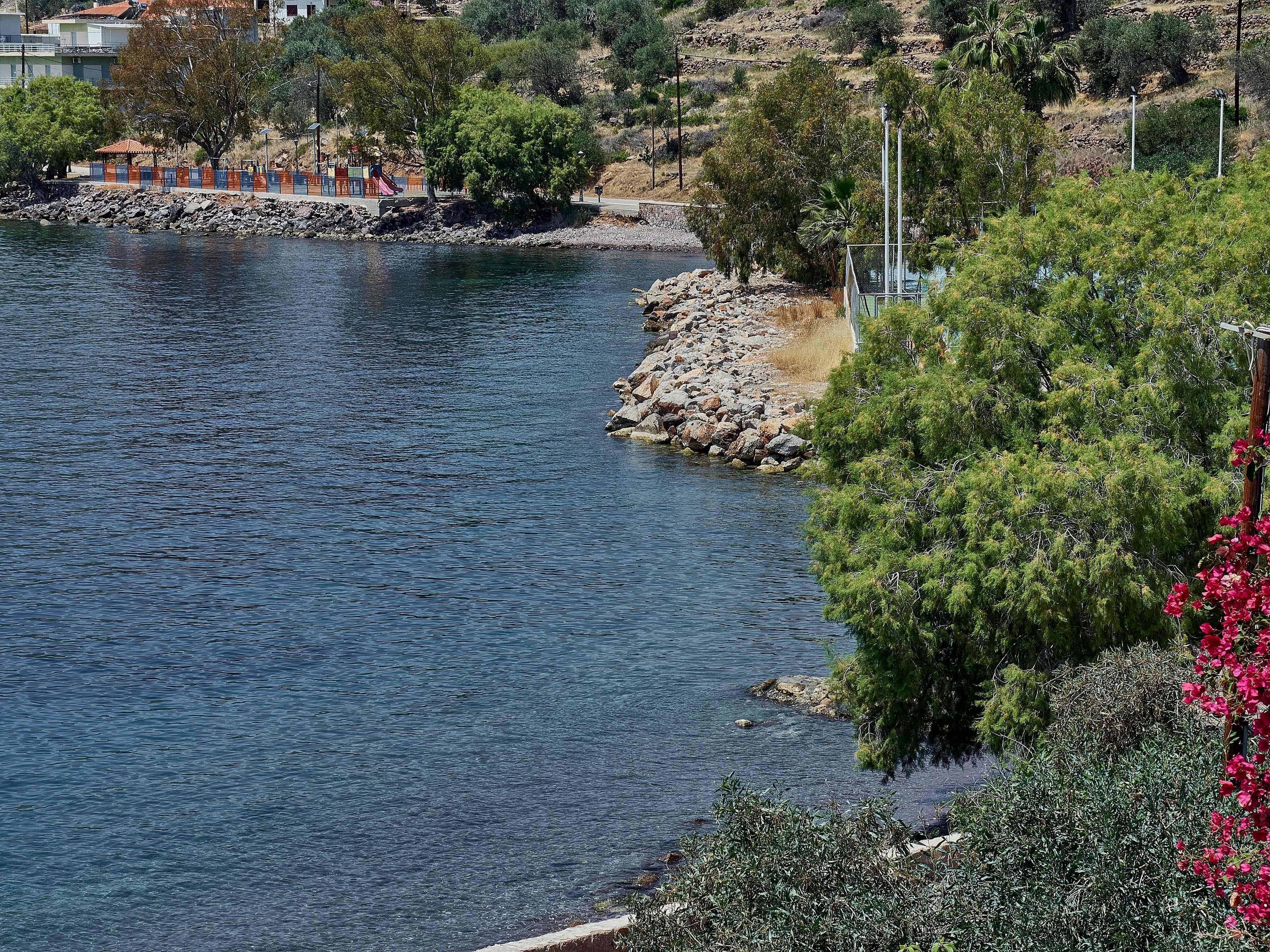 Un fiume con una riva rocciosa, alberi e un edificio sullo sfondo.