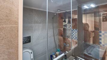 A bathroom with a glass-enclosed shower, a toilet, and a sink with toiletries.