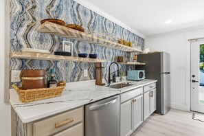 A modern kitchen with marble backsplash, stainless steel appliances, and open shelving. - Court Yard Suite | Pool | Downtown ILM (Wilmington)