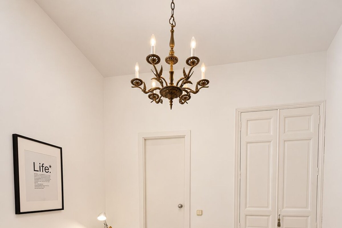 A bedroom with a bed, a chandelier, a framed picture on the wall, and a door.