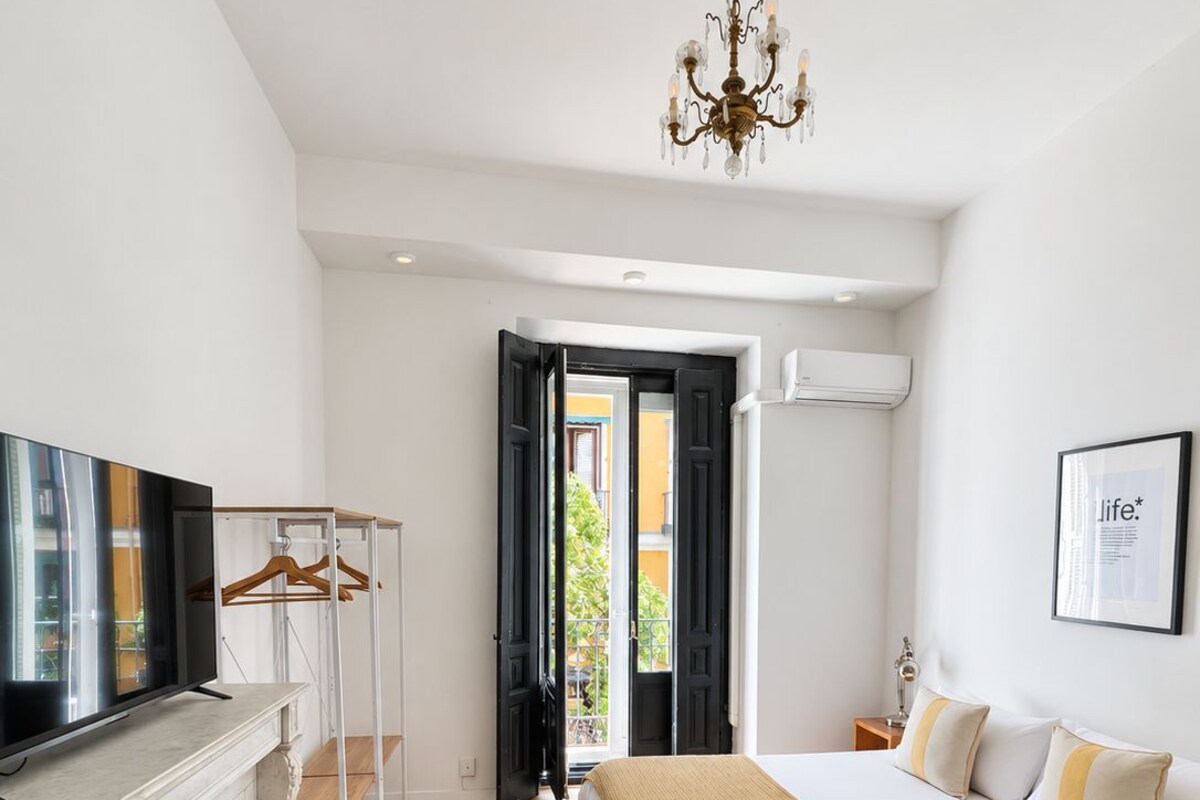 A bedroom with a bed, a television, a fireplace, and an open door leading outside.