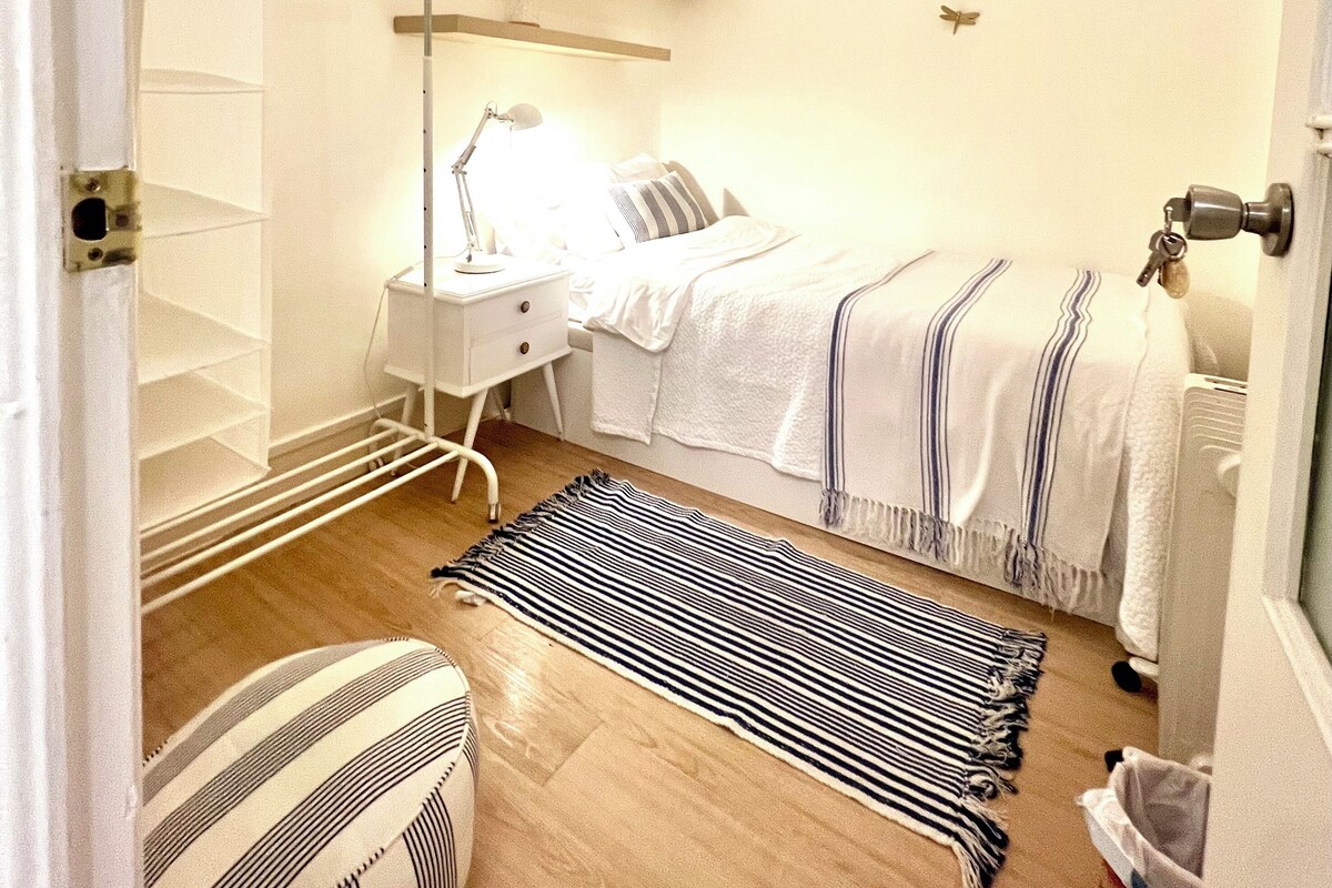 A bedroom with a bed, bedside table, lamp, and a striped rug.
