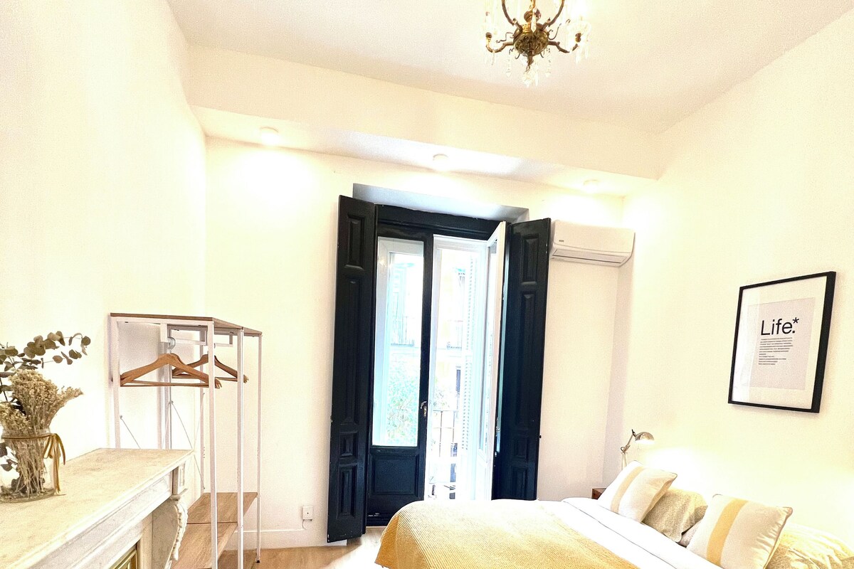 A hotel room with a bed, a dresser, a mirror, a hanging light fixture, and a door leading to a balcony.
