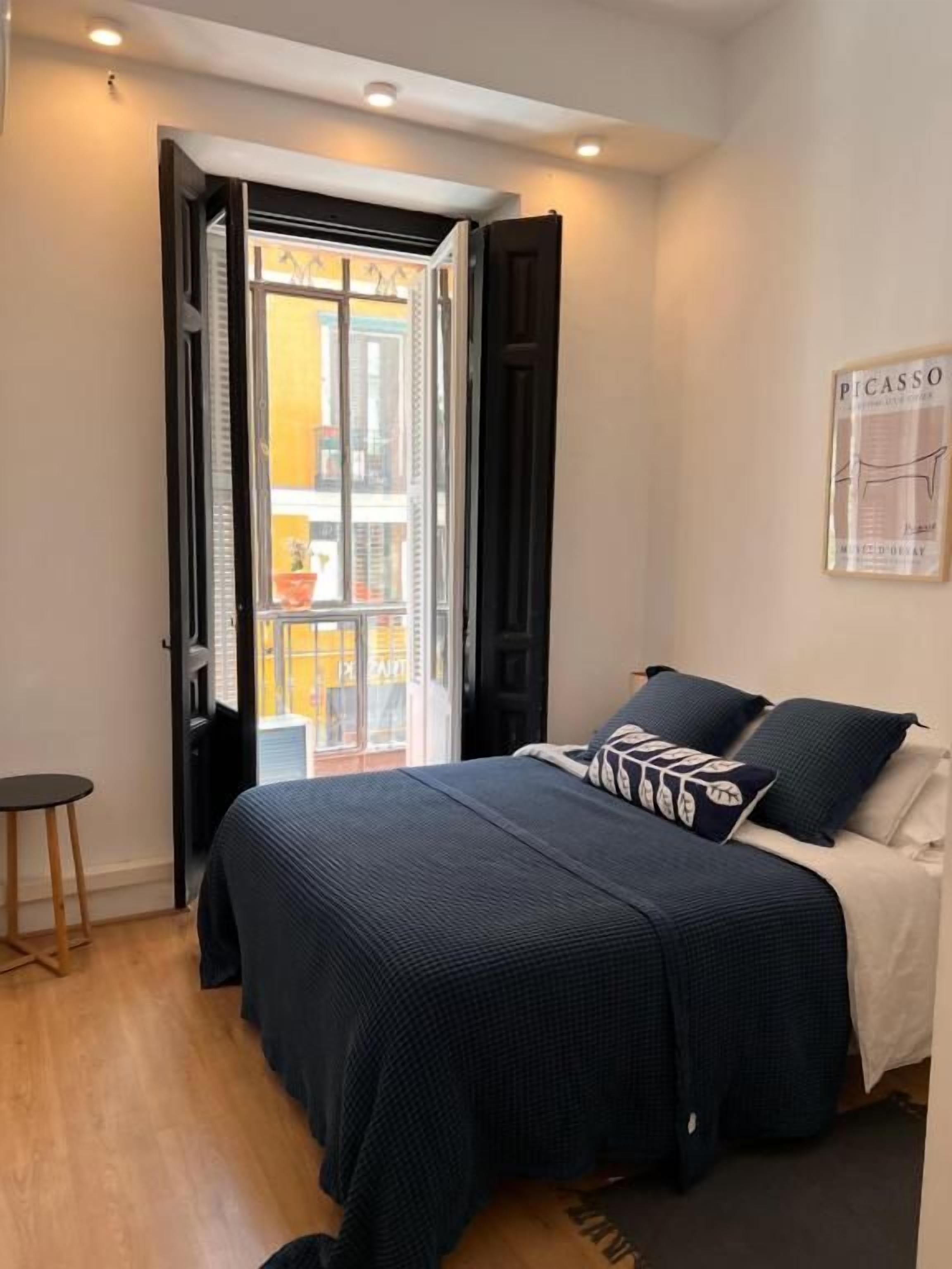 A bedroom with a bed, a door leading to a balcony, and a framed artwork on the wall.