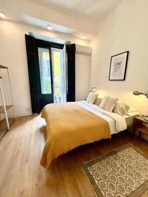 A bedroom with a bed, a bedside table, a lamp, a framed picture on the wall, and a window with curtains. - Fuencarral rooms & stay  (MADRID)