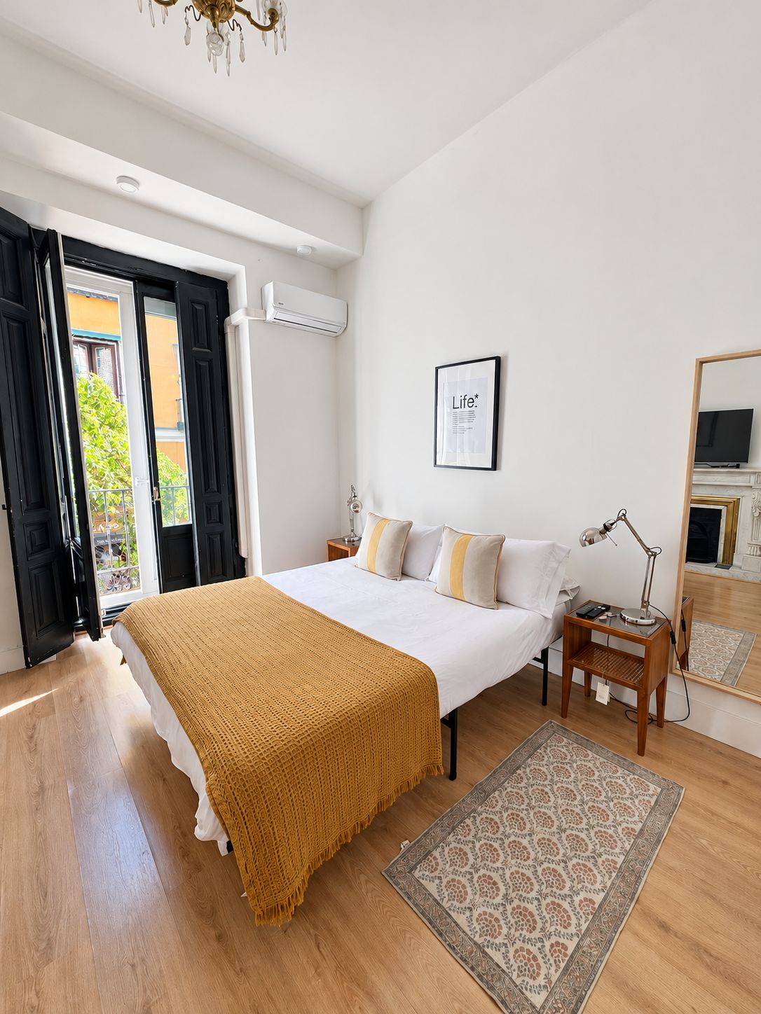 Un dormitorio con cama, mesita de noche, lámpara, aire acondicionado y un cuadro en la pared.
