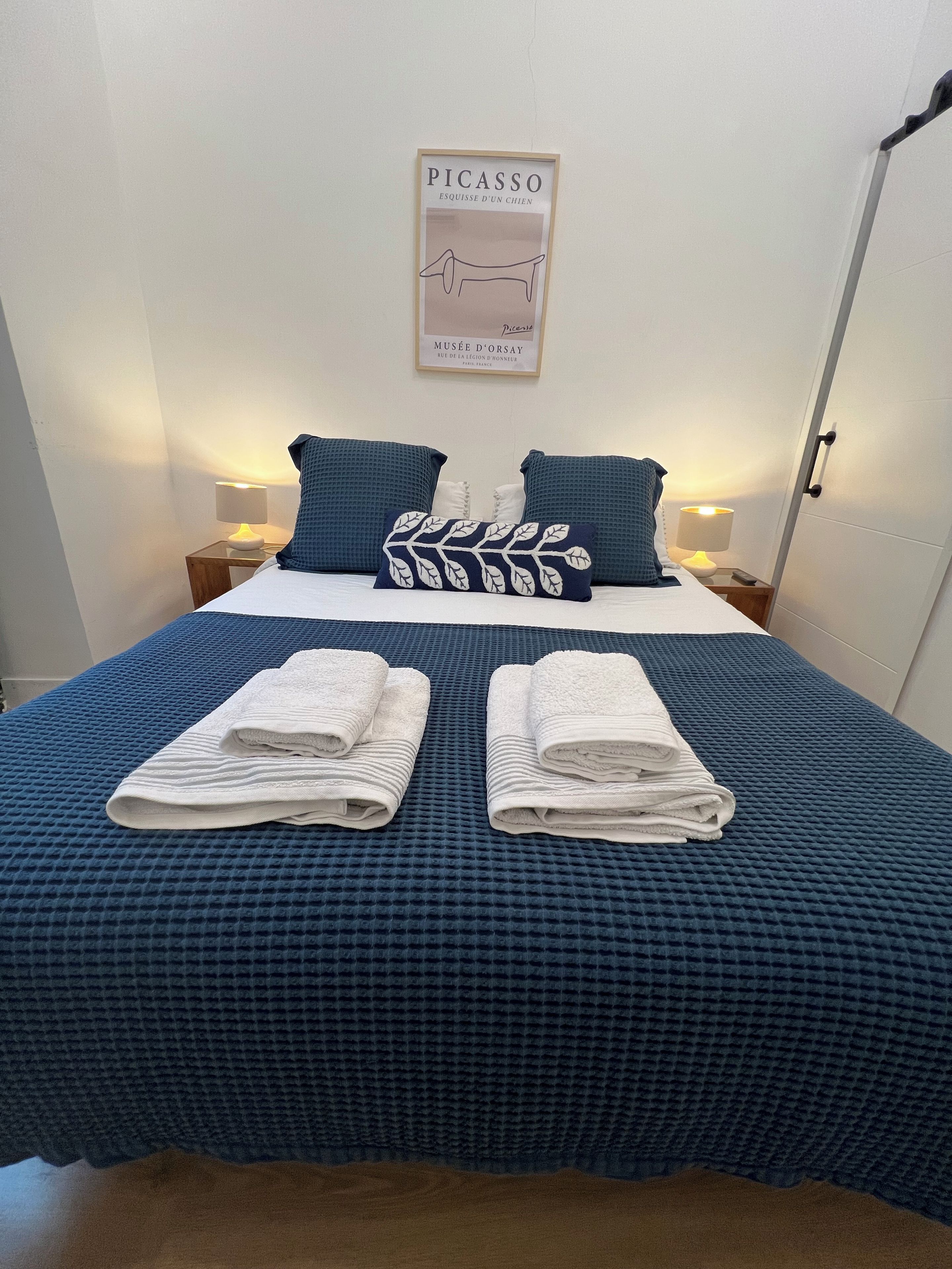 Ein ordentlich gemachtes Bett mit einer blau karierten Bettdecke, zwei Kissen und zwei gefalteten Handtüchern.