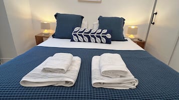 Ein ordentlich gemachtes Bett mit einer blau karierten Bettdecke, zwei Kissen und zwei gefalteten Handtüchern.