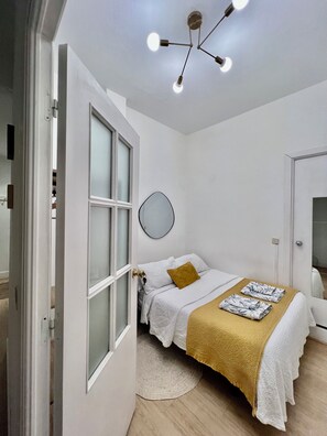 A bedroom with a bed, a round mirror, a ceiling light fixture, and a door.