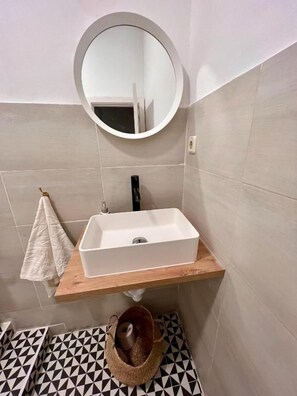 A bathroom with a white sink, a round mirror, and a patterned floor. - Fuencarral rooms & stay  (MADRID)