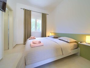 A bedroom with a bed, pillows, a bedside table with a lamp, a window with curtains, and a TV mounted on the wall. - Holiday Home in Pinezici With Swimming Pool (Krk)