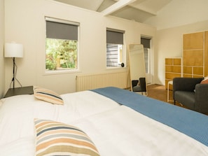 Ein Schlafzimmer mit einem Bett, einem Sessel, einer Lampe und einem Fenster mit Jalousien.