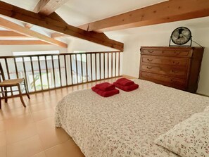 Ein Schlafzimmer mit einem Bett, einem Schminktisch, einem Sessel und einem Balkon mit Geländer.