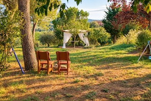 Un espacio al aire libre con dos sillas de madera, una mesa de picnic y un árbol.