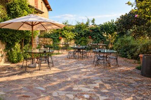 Un patio exterior con suelo de piedra, mesas, sillas y un gran paraguas.