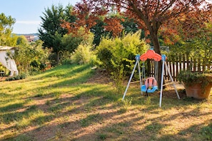 Une balançoire installée dans une cour verdoyante, avec des arbres et une clôture en bois en arrière-plan.