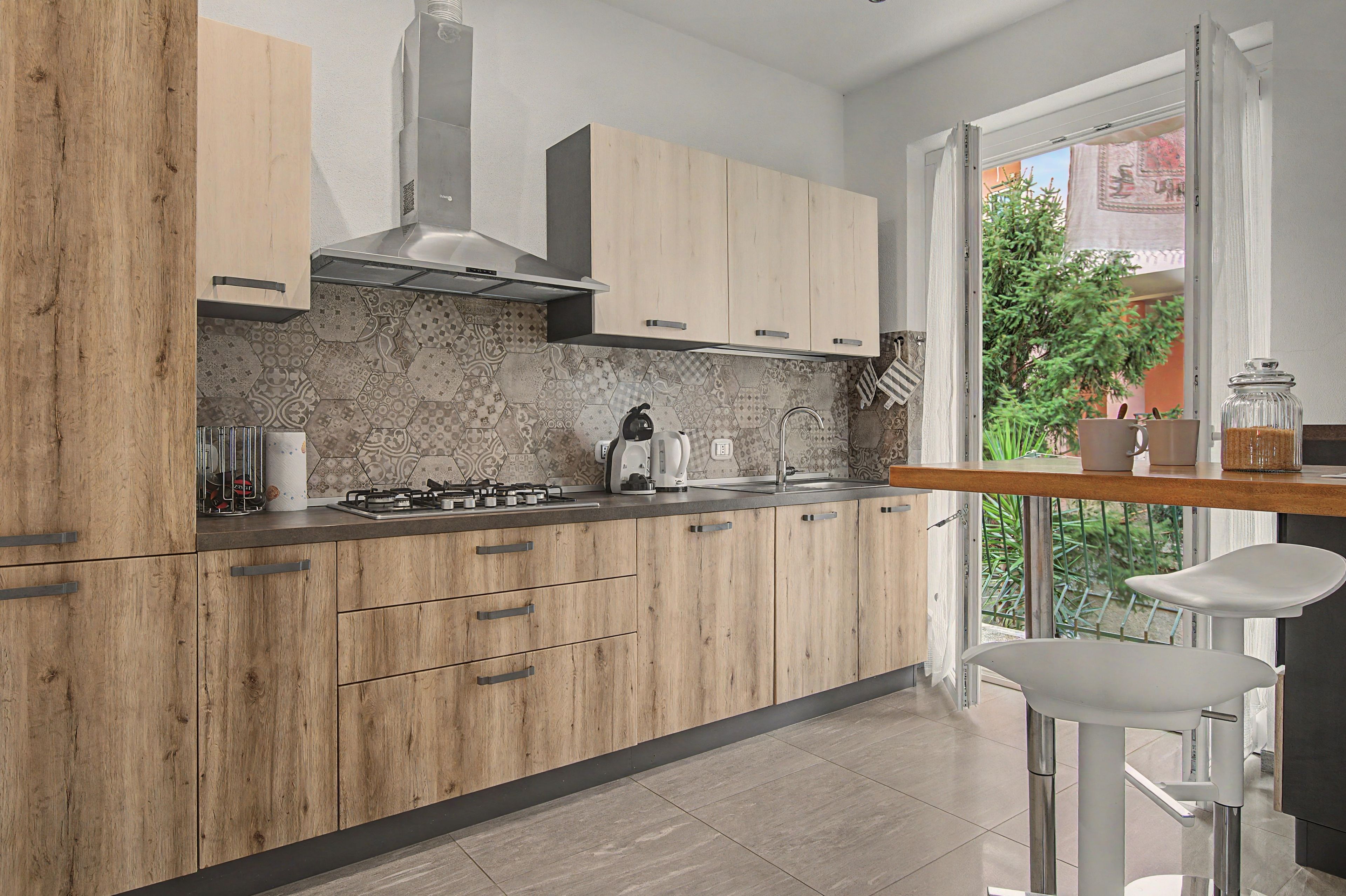A modern kitchen with wooden cabinets, a gas stove, and a view of greenery outside.