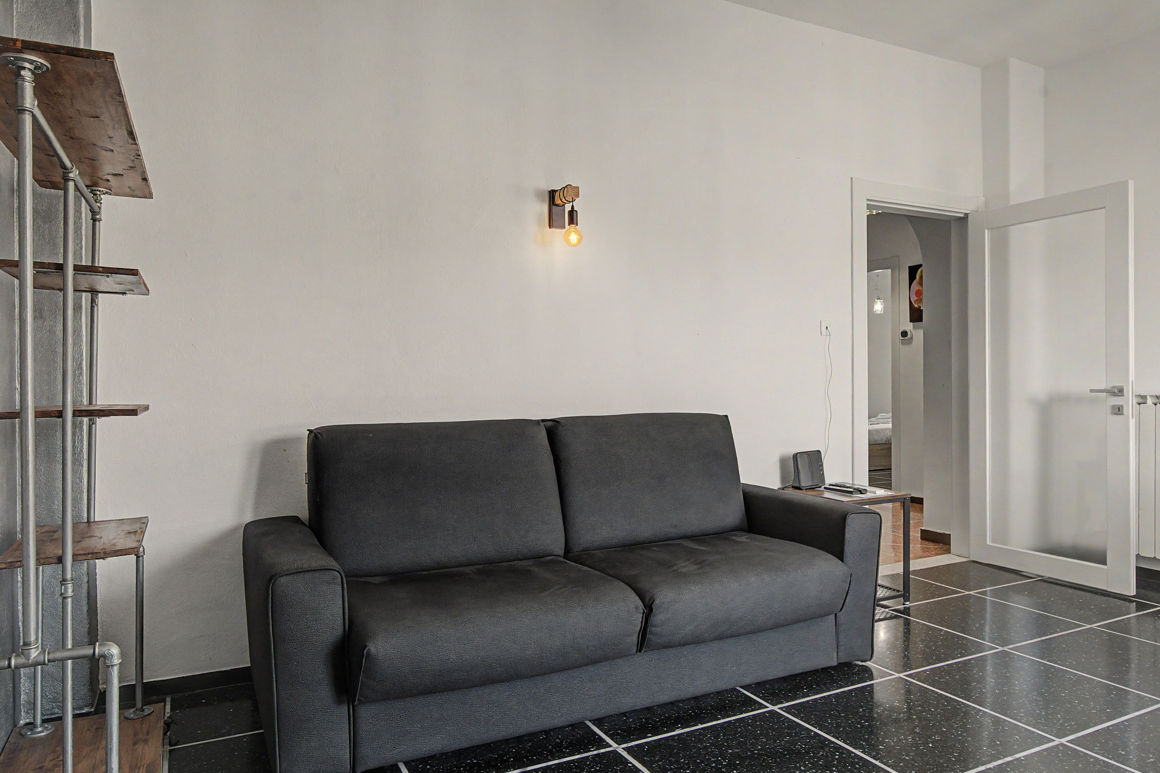 Ein modernes Wohnzimmer mit einem dunkelgrauen Sofa, einem Metallregal und einer Wandleuchte.