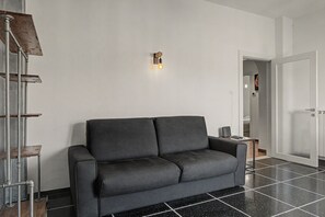 Un saló modern amb un sofà gris fosc, un moble prestatge metàl·lic i una làmpada penjant a la paret.