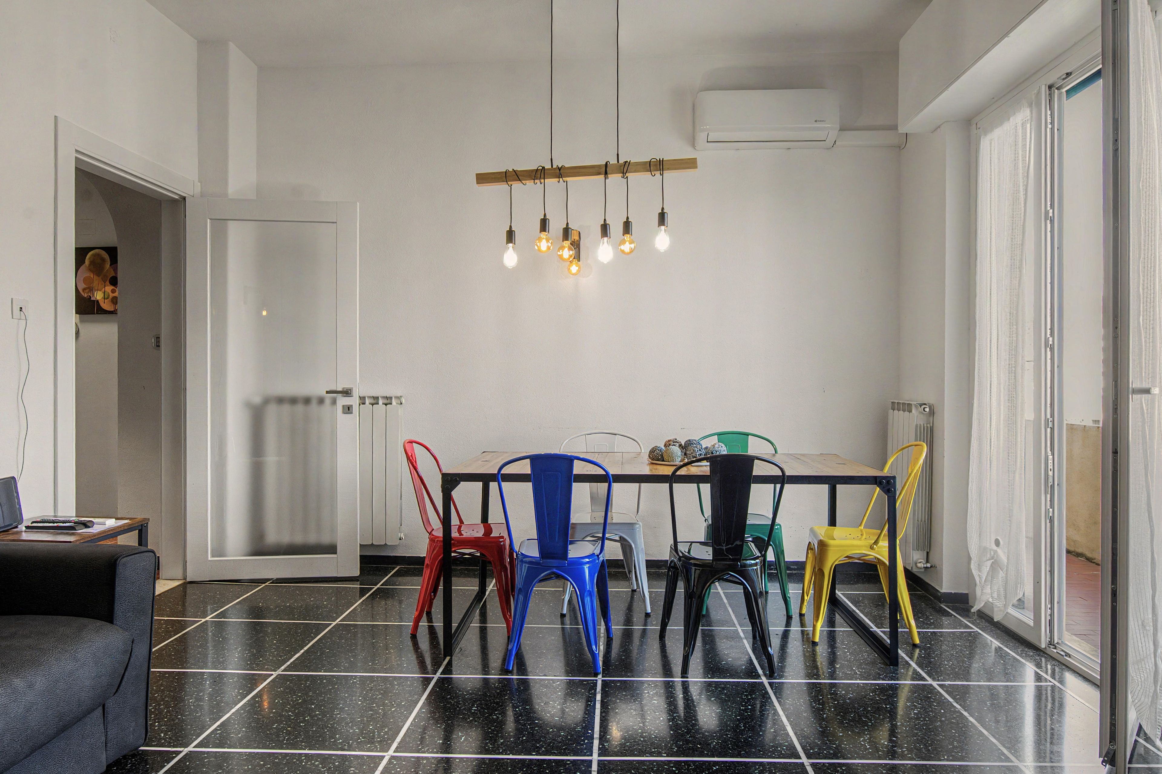 A dining area with a black tiled floor, a wooden table, and colorful chairs.