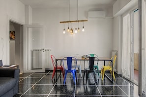 Zona de menjador amb un sòl de rajoles negres, una taula de fusta i cadires de colors.