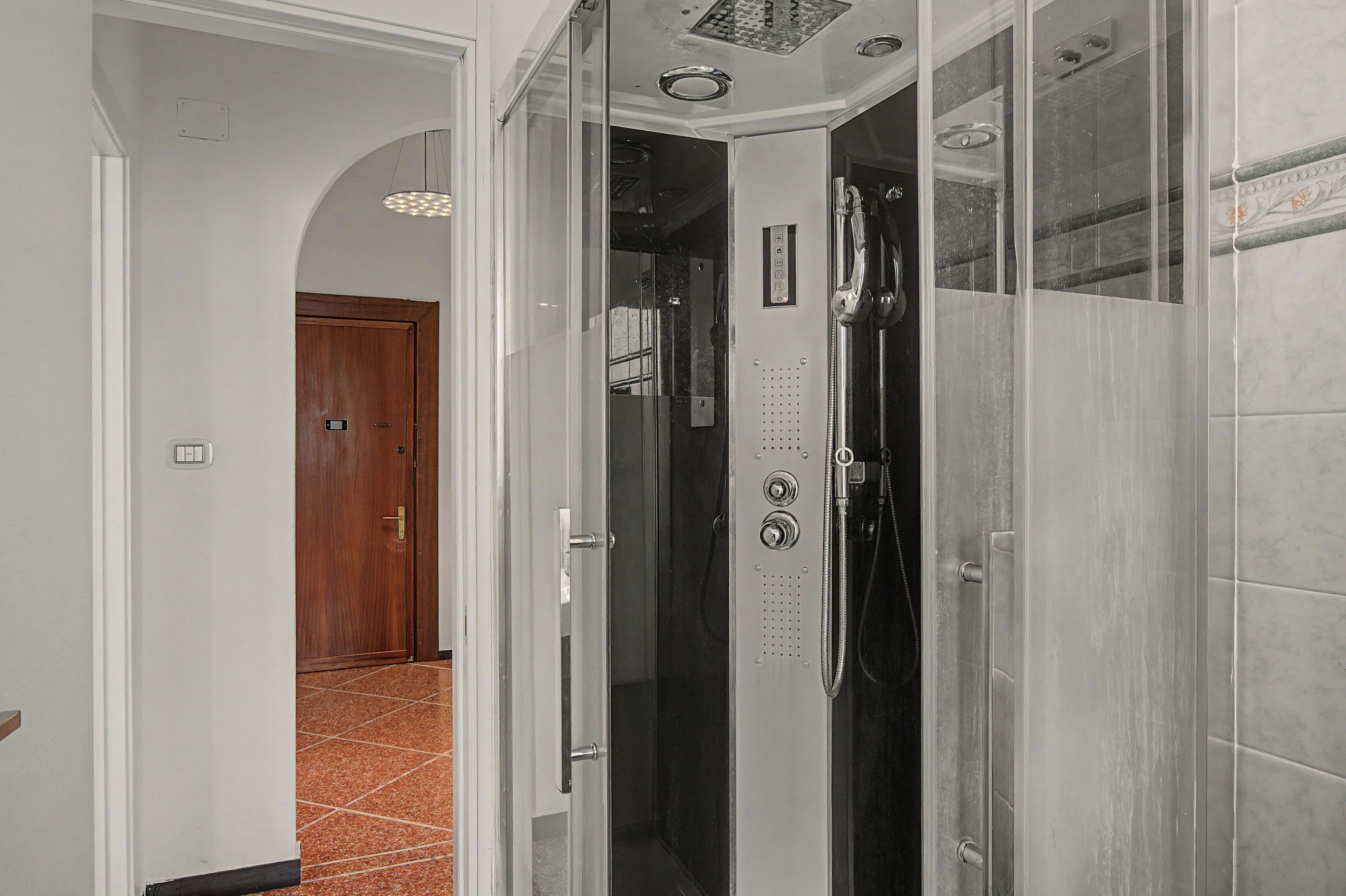 A bathroom with a glass shower enclosure, a visible control panel, and a door leading to another room.