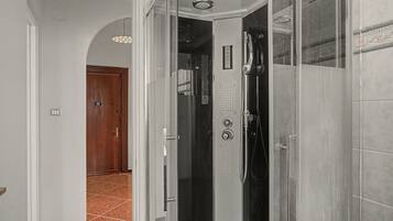 A bathroom with a glass shower enclosure, a visible control panel, and a door leading to another room.