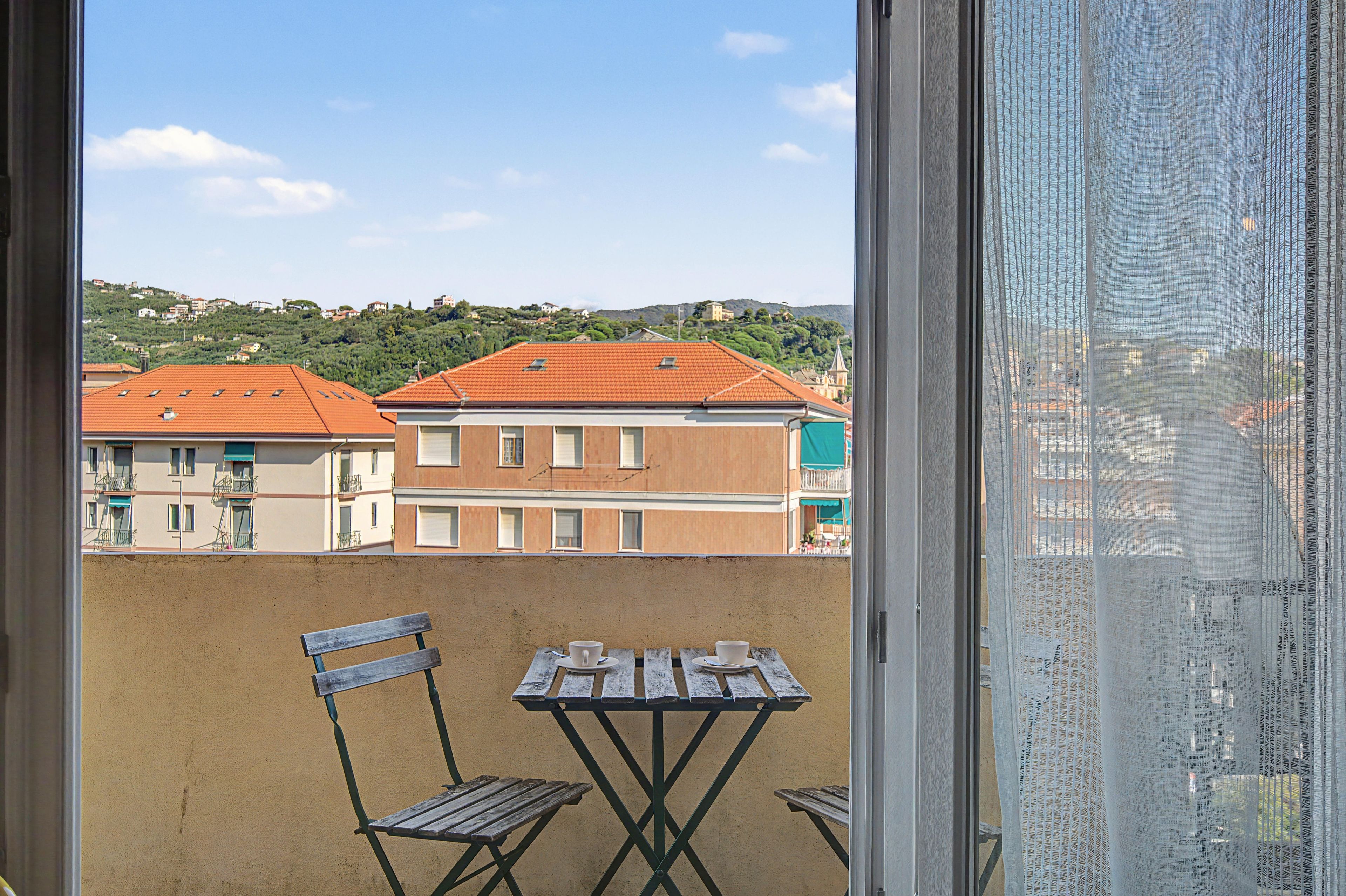 Un balcón con mesa y sillas, con vistas a una zona residencial con edificios y una colina.