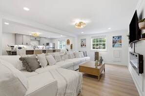 A modern living room with a sofa, coffee table, and kitchen in the background. - Ibiza Bohemia | Pool | Downtown ILM (Wilmington)