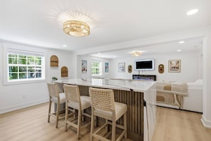 Een moderne keuken met een centraal eiland, barstoelen, een flatscreen televisie en een groot raam.