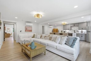 A modern living room with a white sofa, a wooden coffee table, and a kitchen area in the background. - Ibiza Bohemia | Pool | Downtown ILM (Wilmington)