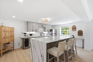 Een moderne keuken met een centraal eiland, witte kasten en een groot raam dat voor veel daglicht zorgt.